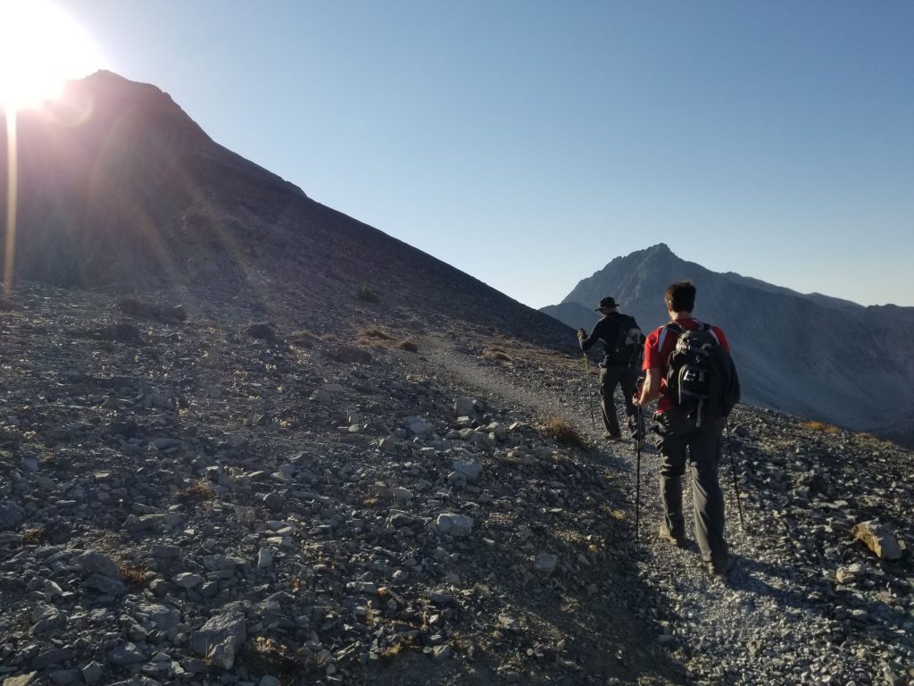 Two hikers ascending a good trail as the morning sun shines over the shoulder of the mountain