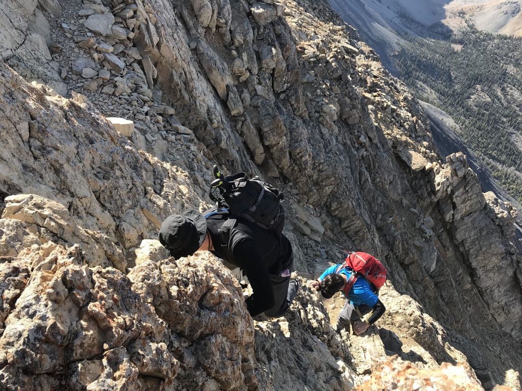 A daring downclimb scramble on rock while mountain climbing by two climbers. 